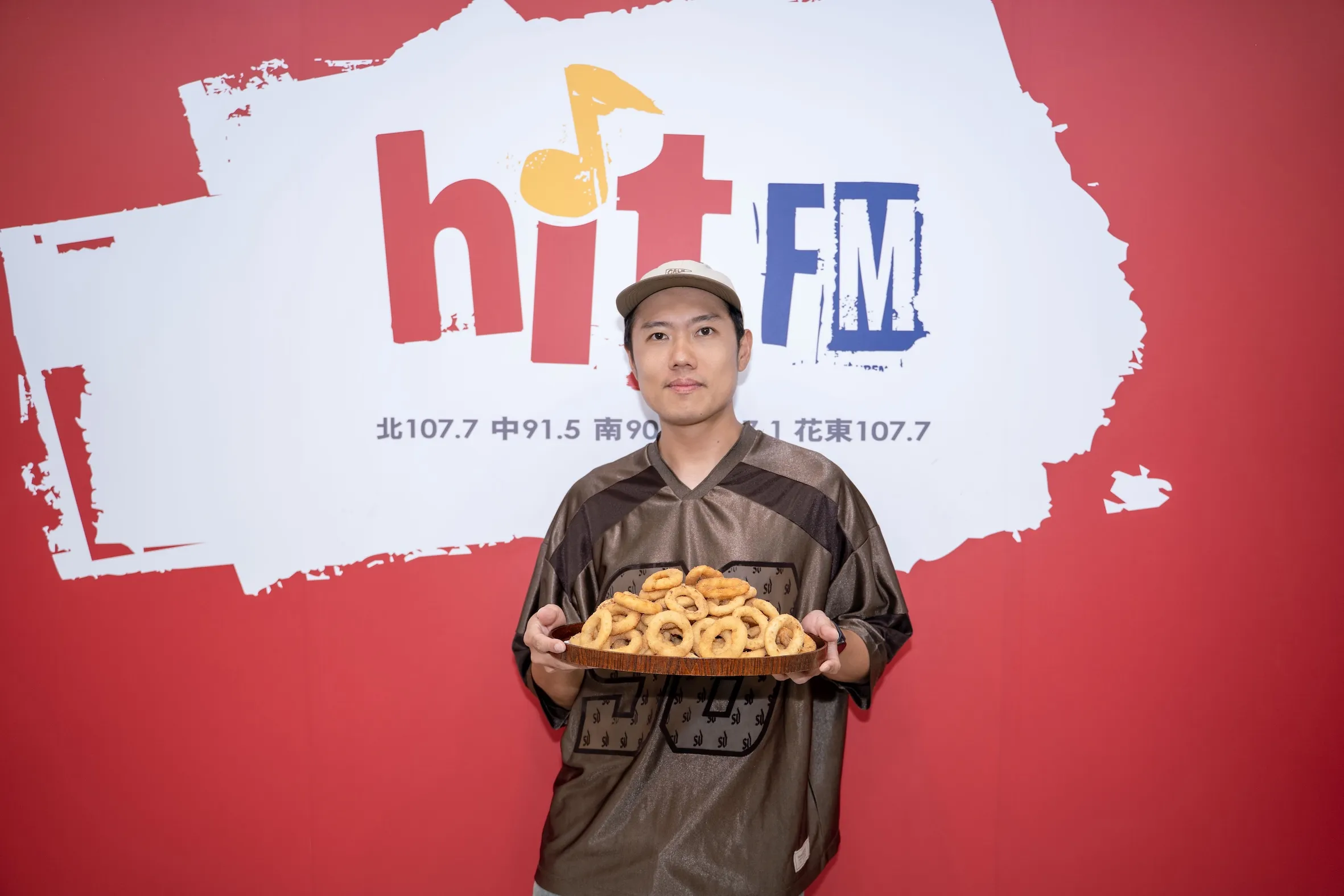玖壹壹團員洋蔥現身Hit Fm聯播網宣傳全新單曲，接受「耐玩DJ」Bryan贈送的炸洋蔥圈。（圖／Hit Fm聯播網提供）